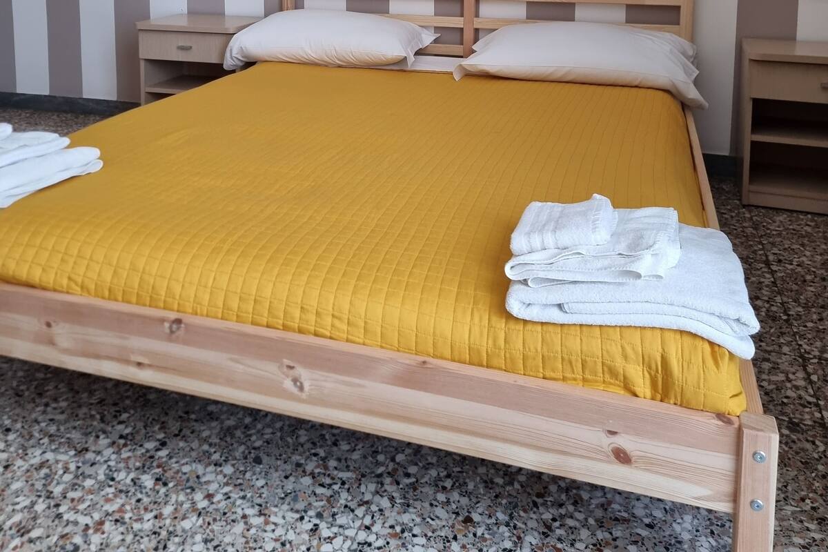 A bed with a wooden frame, a yellow quilted bedspread, and white pillows. There are two bedside tables with lamps.