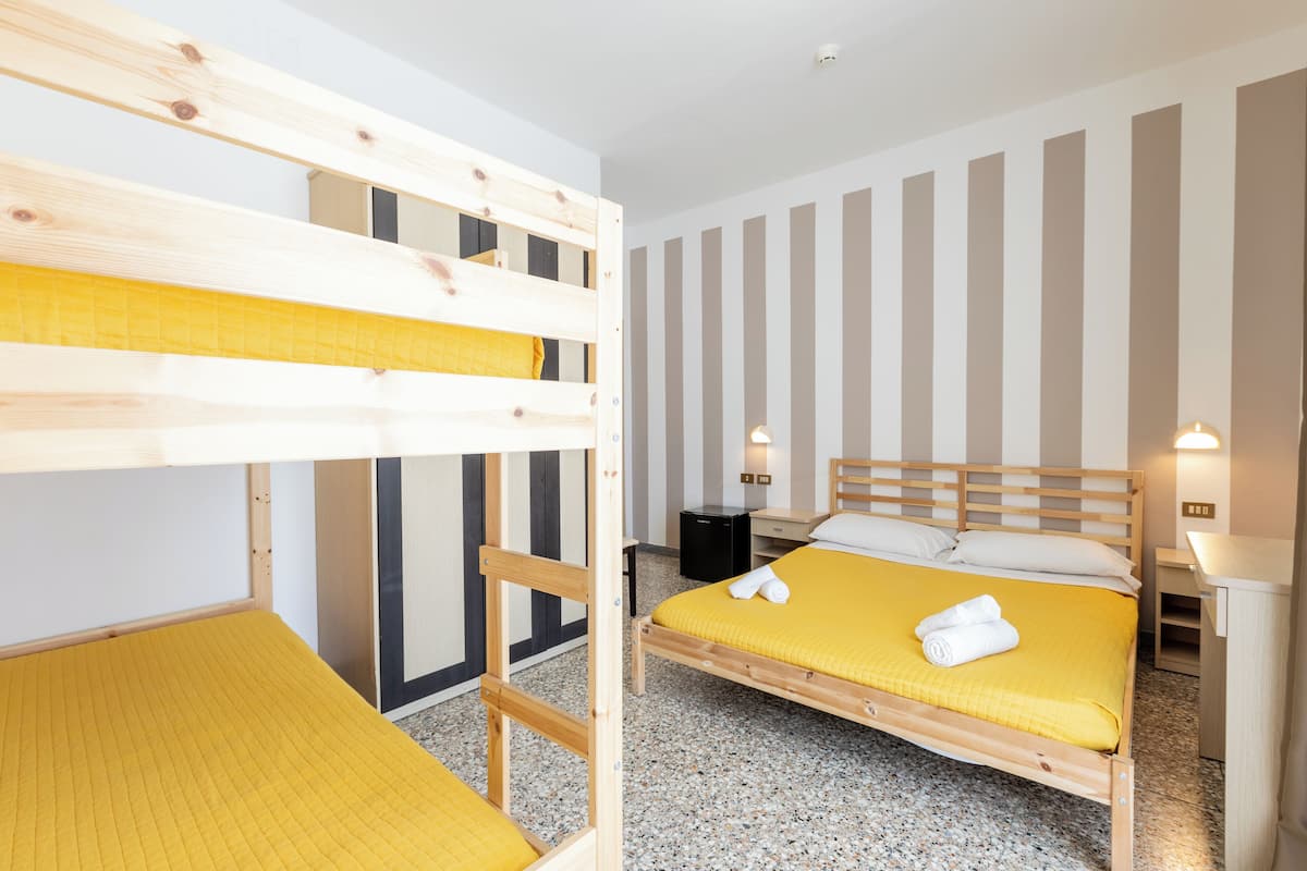 A bunk bed room with a yellow mattress, a wooden headboard, and a bedside table with a lamp.
