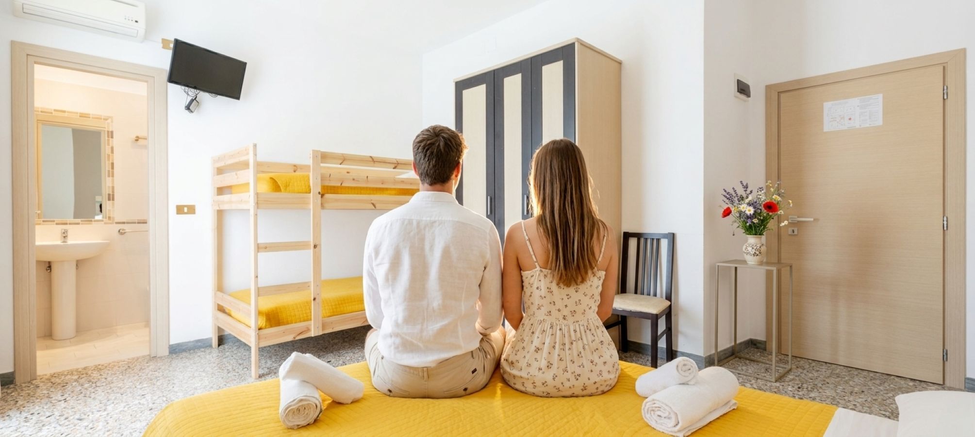 A room with bunk beds, a sink, a chair, a TV, and a door with a notice.