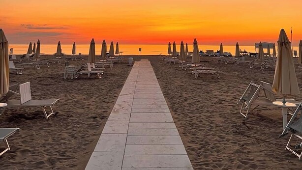 A beach with a paved walkway leading to the water, surrounded by beach chairs and umbrellas. - Beach Hotel Clerice (Rimini)