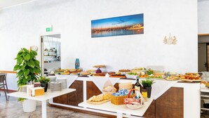 A buffet setup with various food items, a potted plant, and a painting of a cityscape on the wall. - Beach Hotel Clerice (Rimini)