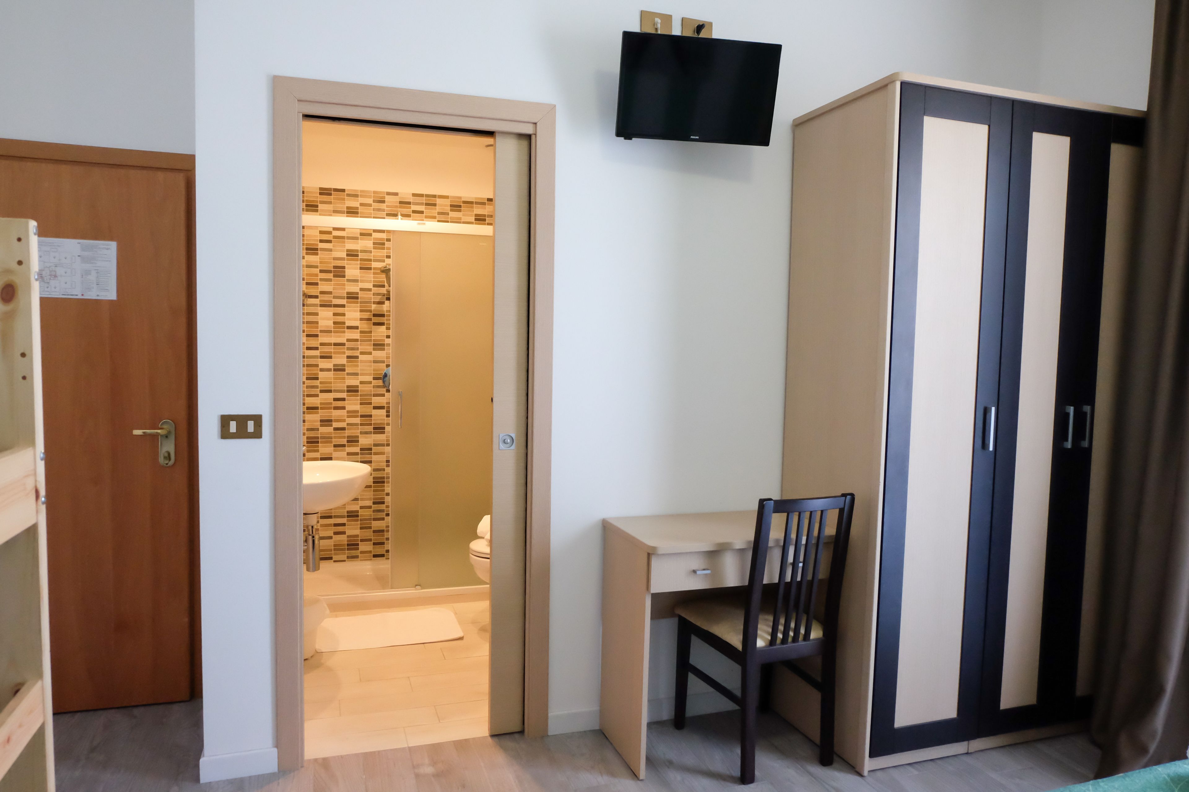 Une pièce avec une porte en bois, un bureau avec une chaise, une armoire et une salle de bain visible à travers une porte ouverte.