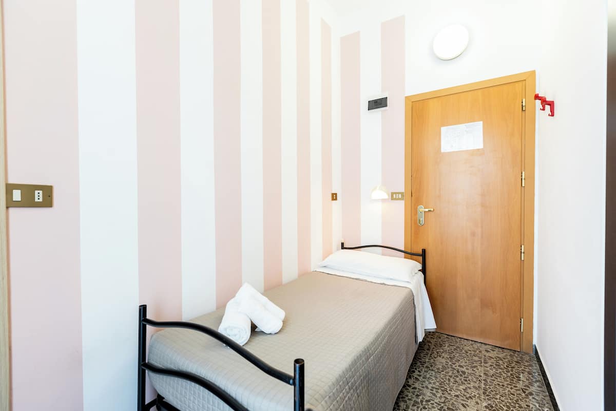 A single bed with a headboard, a wooden door, and a striped wall.