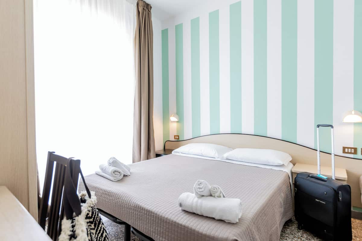 A hotel room with a bed, a suitcase, and a chair.