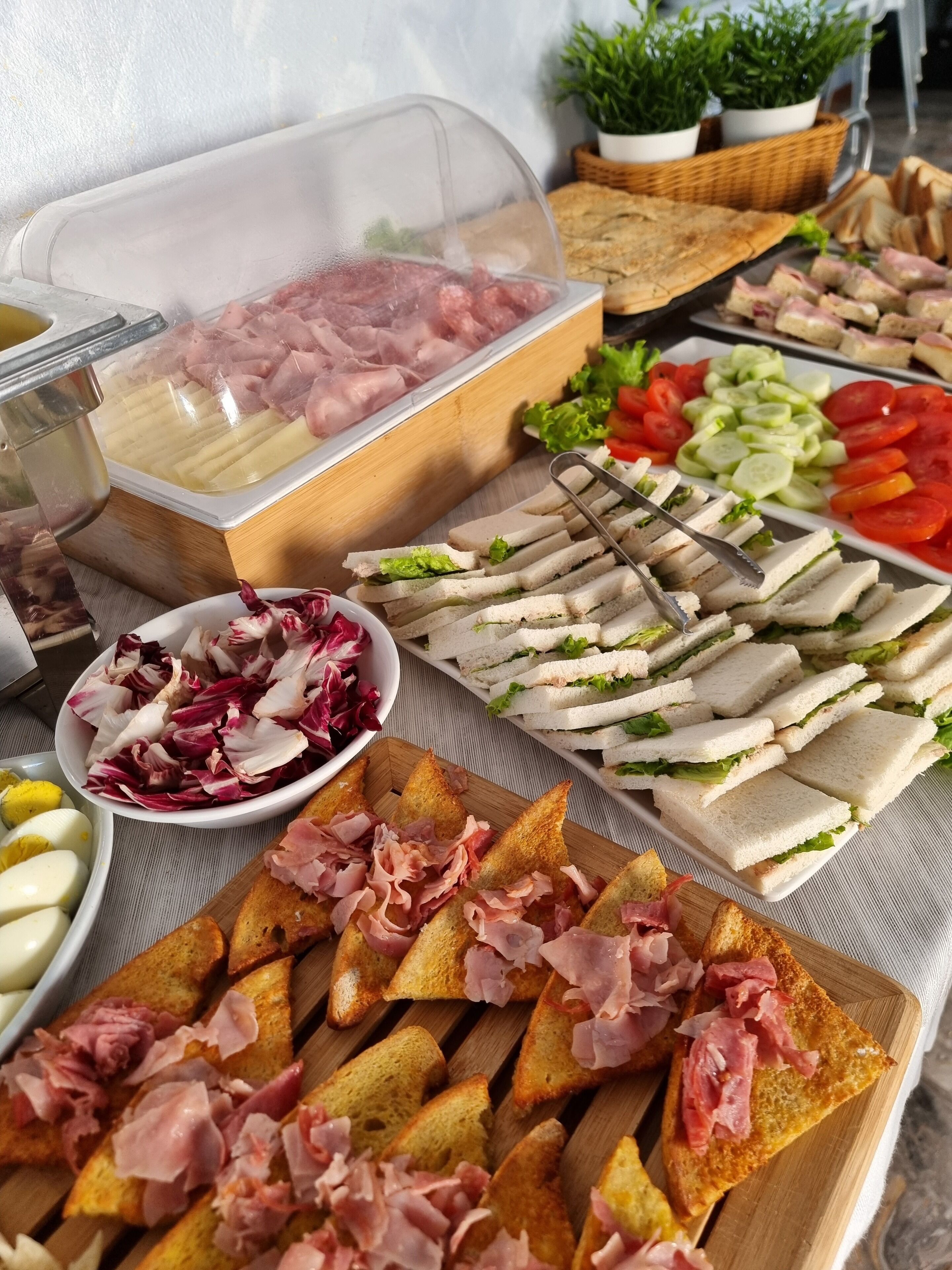 A buffet with various food items including sandwiches, sliced cucumbers, tomatoes, and bread with ham.