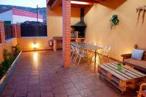 An outdoor patio with a brick wall, a wooden table, chairs, a barbecue grill, and a sofa.
