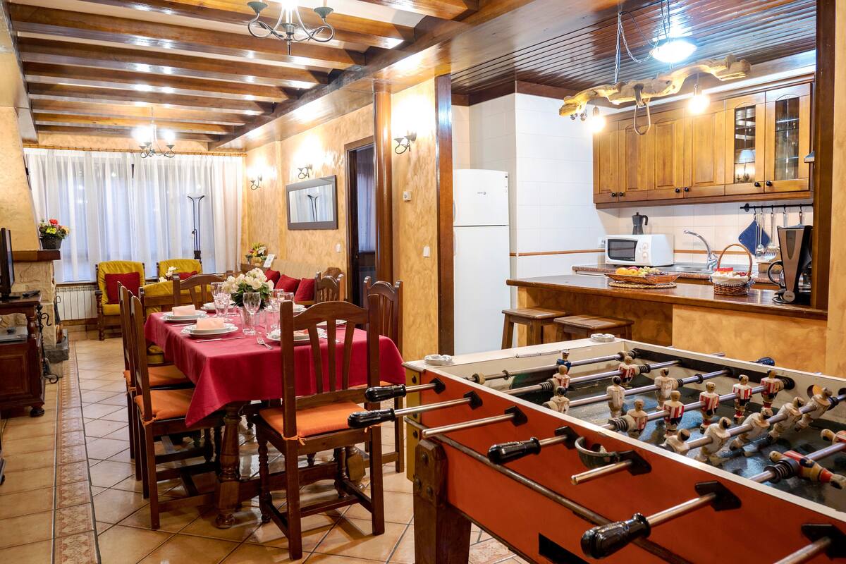A dining area with a red tablecloth, wooden chairs, and a foosball table.