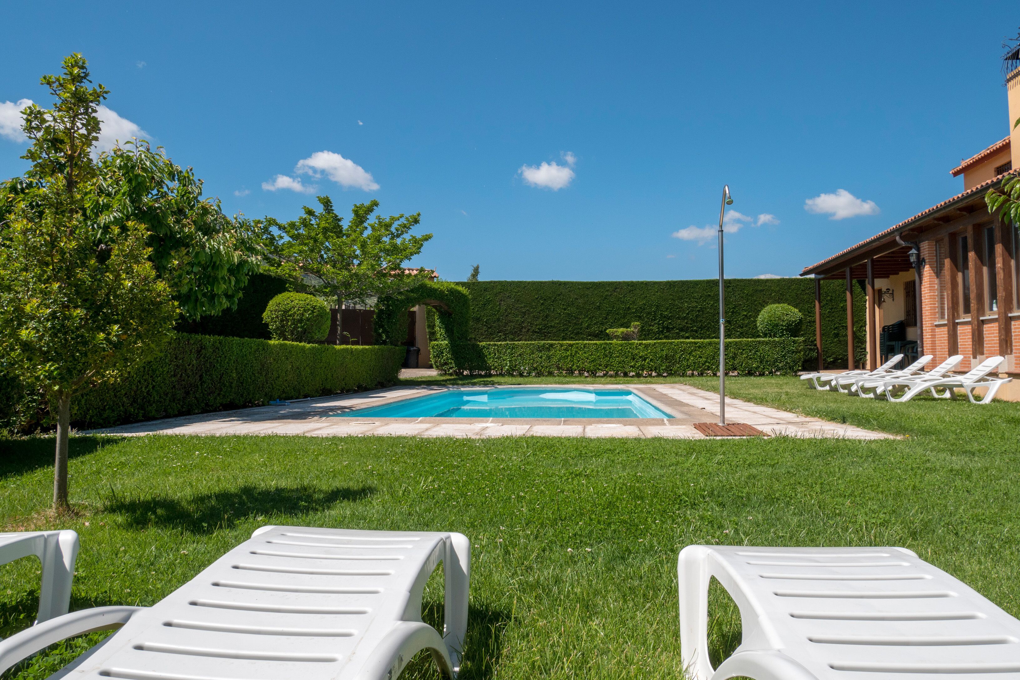 A swimming pool with lounge chairs, surrounded by well-maintained grass and hedges.