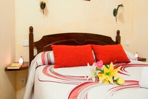 A neatly made bed with red pillows, a bedside table with a lamp, and a floral arrangement on the bed.