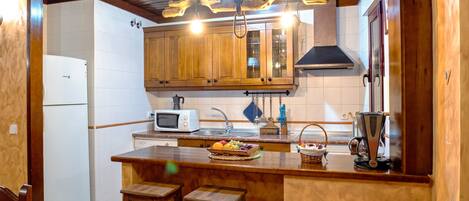 A kitchen with wooden cabinets, a white refrigerator, a microwave, and a fruit basket on the counter.
