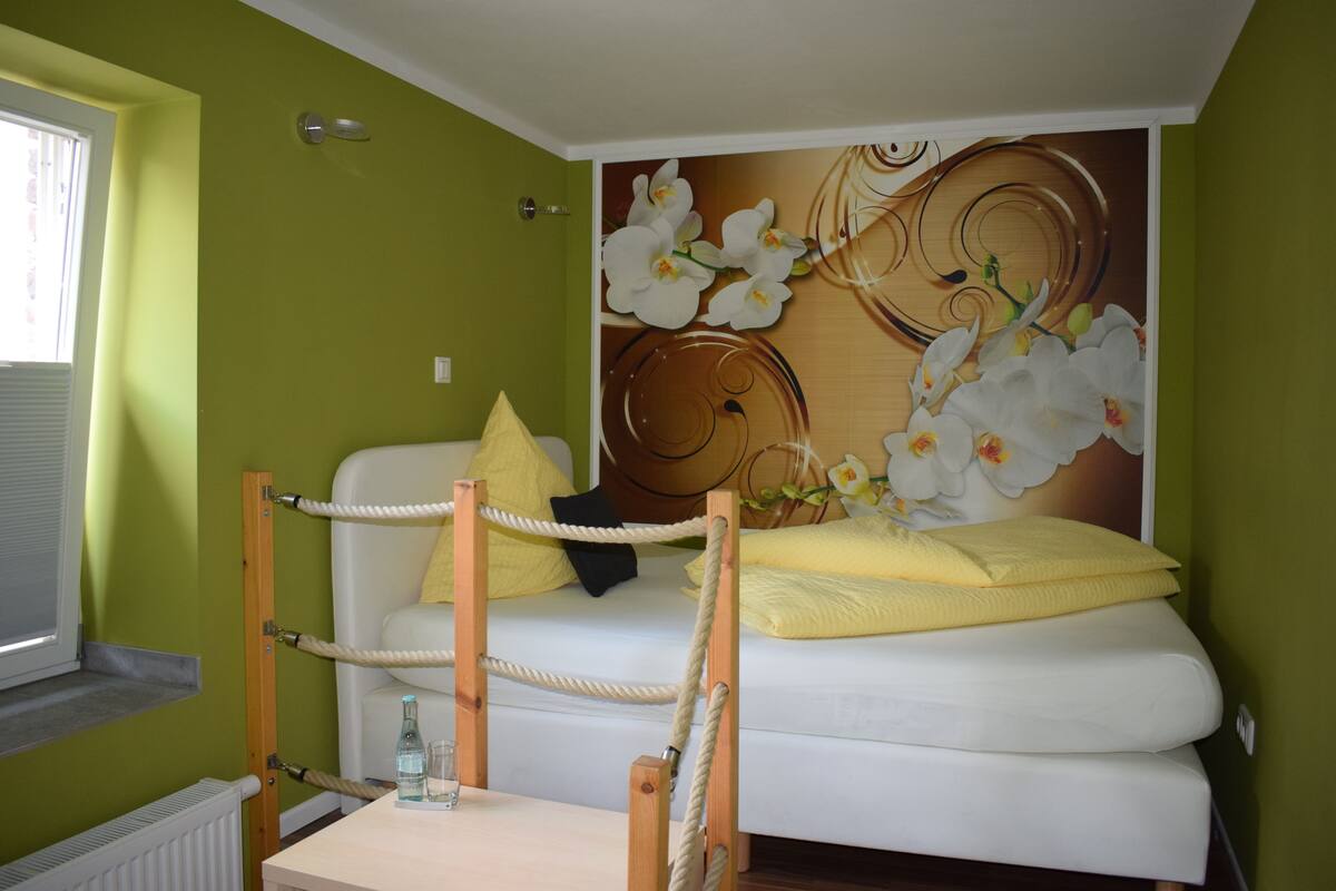 Una habitación con cama, ventana y un mural de orquídeas en la pared.