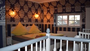 Un dormitorio con cama, barandilla blanca, papel tapiz estampado y ventana con vistas.