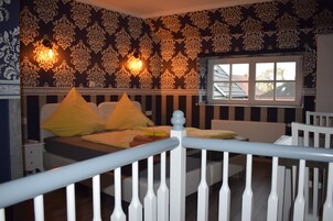 Quarto com cama, corrimão branco, papel de parede estampado e janela com vista.