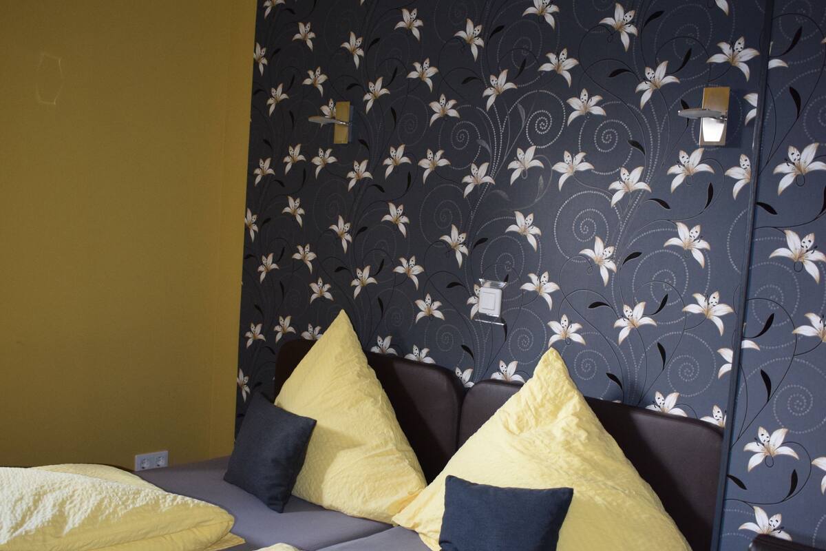 Un dormitorio con cama, almohadas y una pared con estampado floral.
