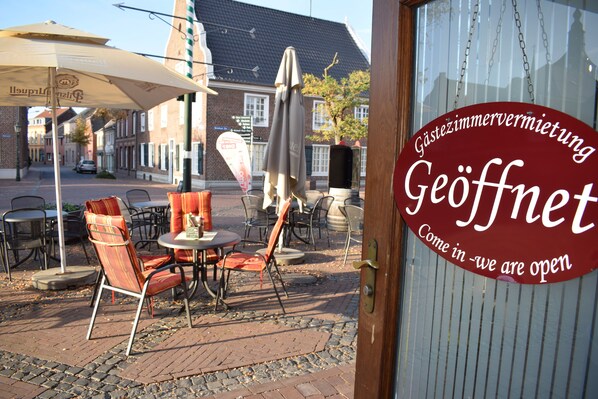 An outdoor seating area with tables and chairs, a sign indicating the establishment is open, and a brick building in the background. - Gast und Weinhaus Zwiebelturm (Kerken)
