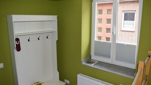 Una habitación con pared verde, un radiador blanco, una ventana con persianas, un armario blanco con ganchos y una toalla roja sobre el mostrador.