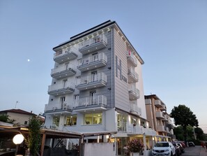 Un hotel de varios pisos con balcones, un restaurante a nivel de calle y coches aparcados.