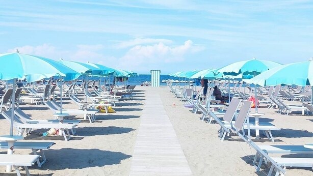 A beach with rows of sun loungers and umbrellas, a wooden walkway, and a clear sky. - Hotel Kim (Rimini)