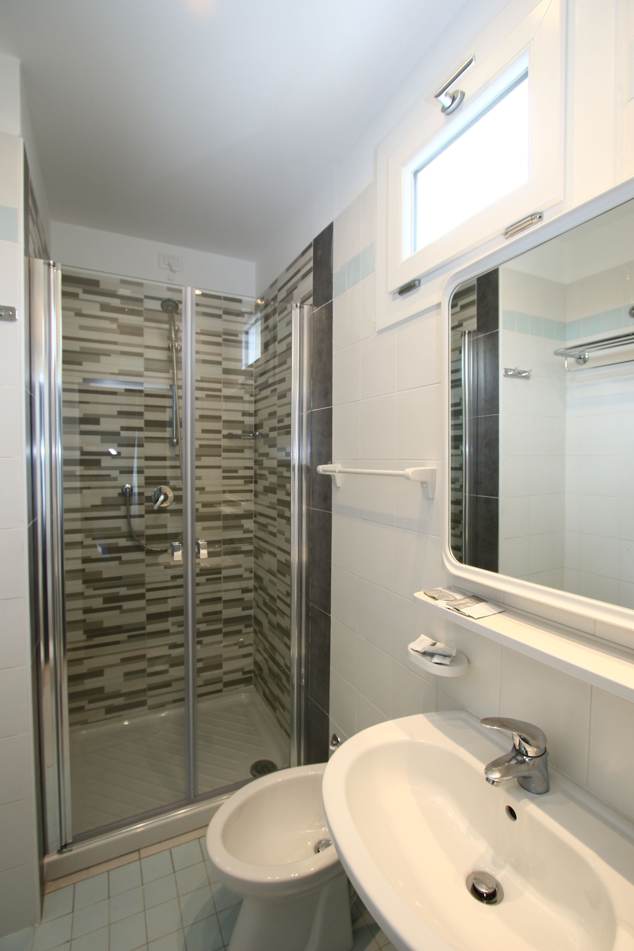 A modern bathroom with a glass-enclosed shower, a white sink, and a large mirror above the sink.