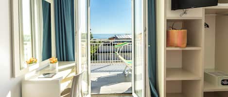 A balcony with a view of the sea, a TV mounted on the wall, and a small table with a vase of flowers.