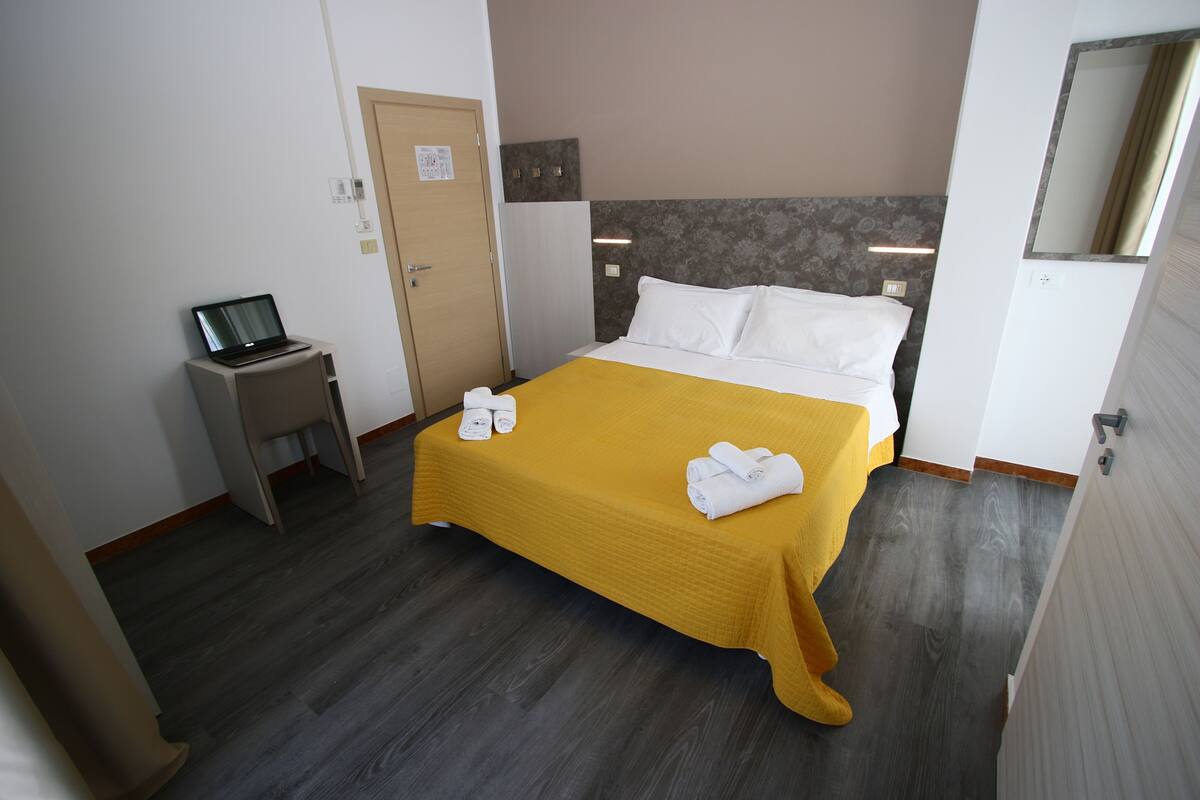 A hotel room with a bed, a desk with a laptop, and a door.