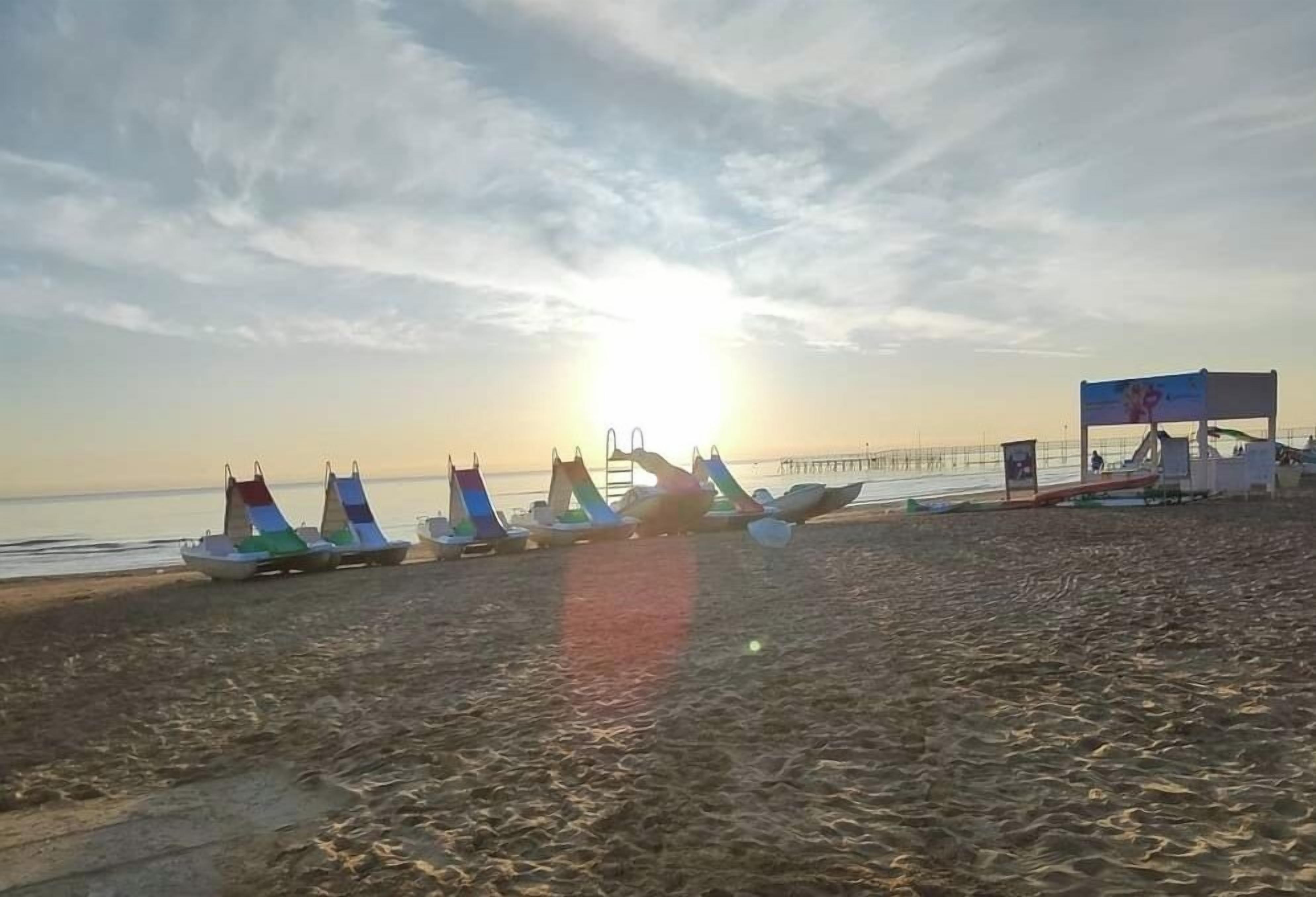 Une plage où plusieurs voiliers sont alignés sur le sable, une jetée en arrière-plan et un ciel dégagé.