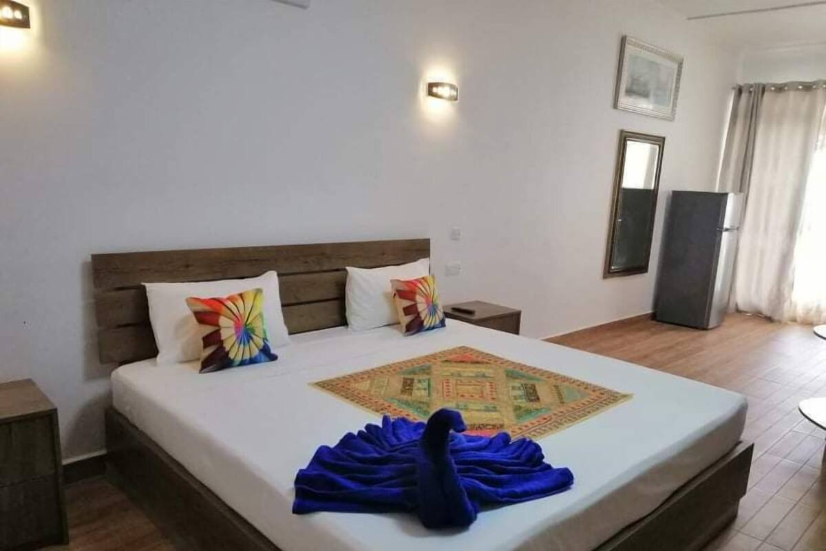 A neatly made bed with a colorful pillow, a blue towel, and a decorative rug.