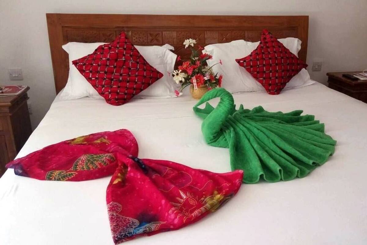A neatly made bed with white sheets, red and green pillows, and a floral arrangement.