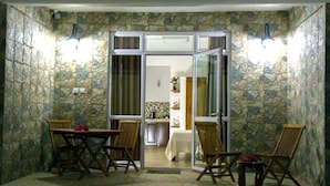 A dining area with a stone wall, a glass door leading to a kitchen, and wooden furniture. - Easy Stay Residence (Trou aux Biches)