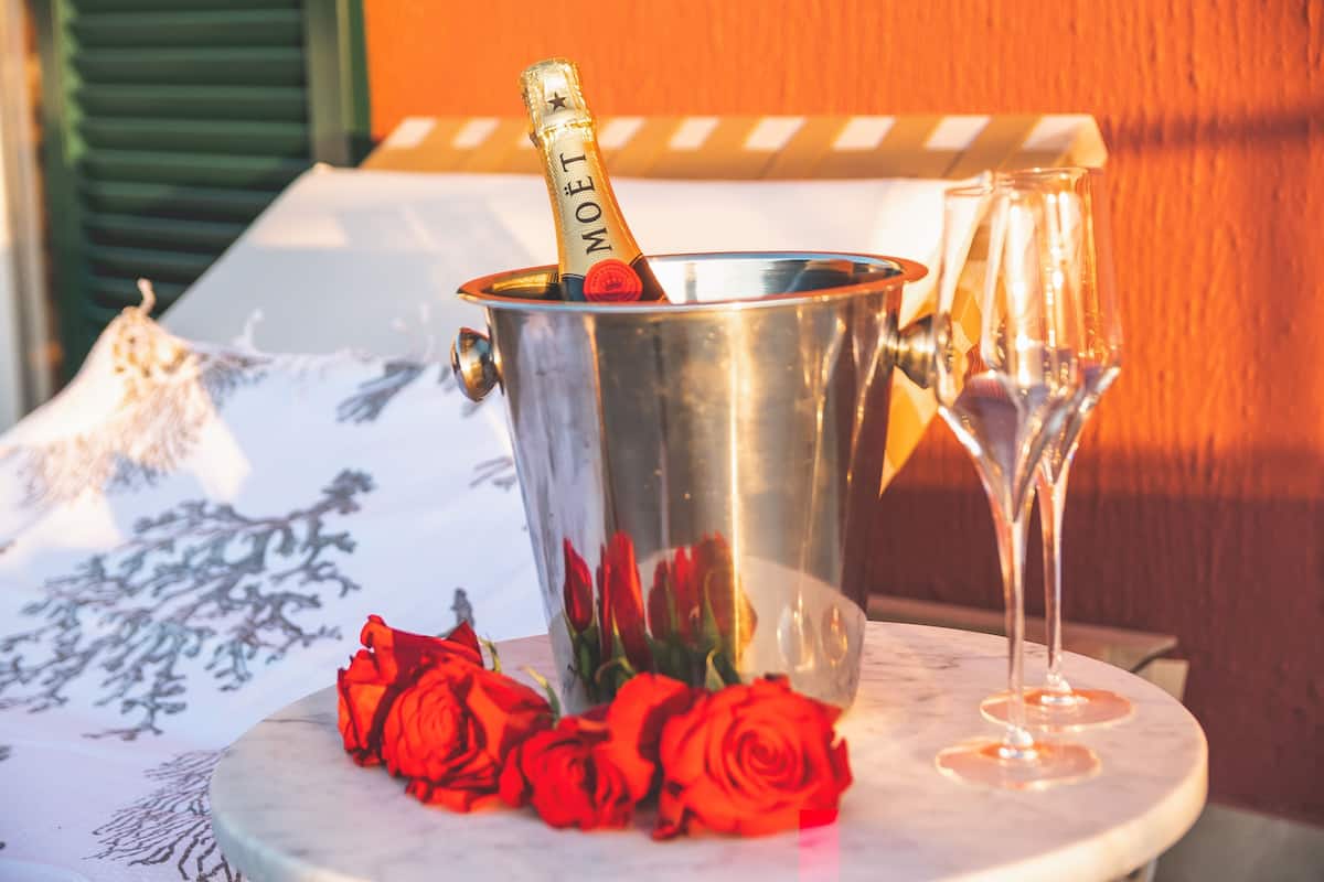 A champagne bottle in a metal bucket, a glass, and red roses on a table.