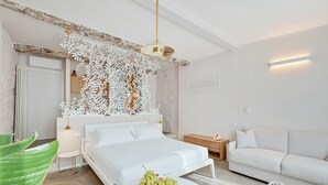 A modern hotel room with a large bed, a white sofa, a small table with fruit, and a decorative wall panel.