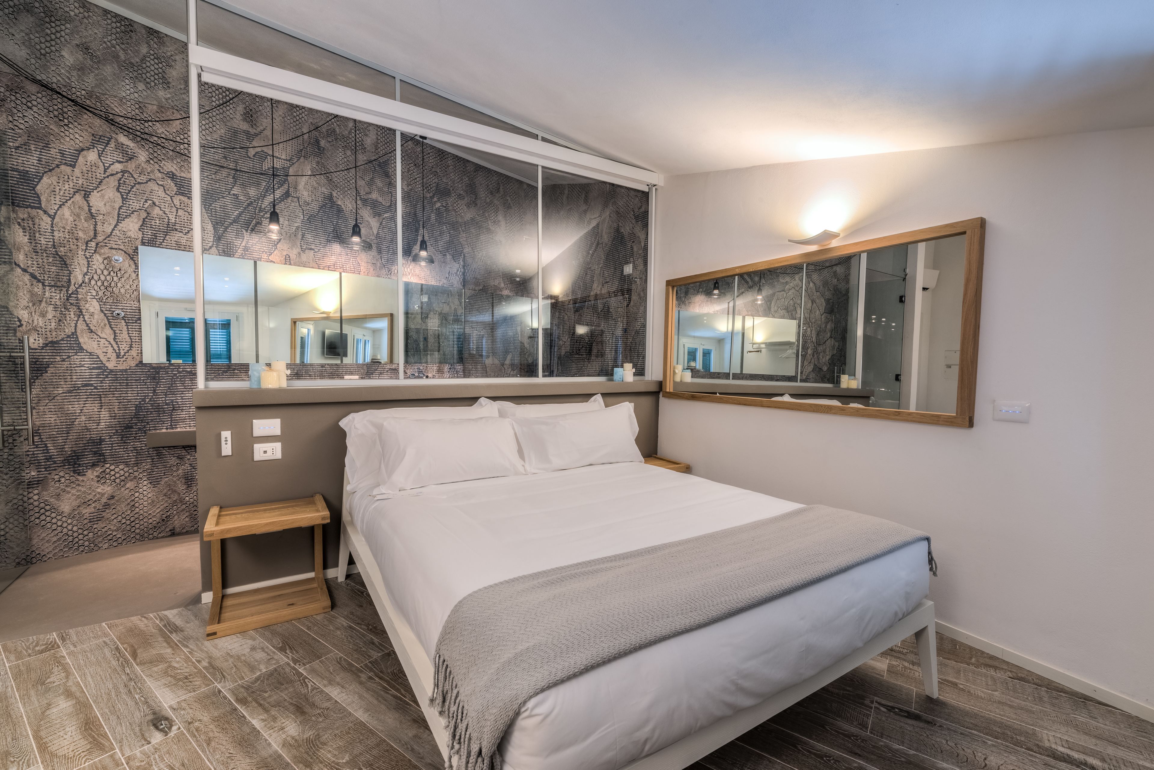 A modern bedroom with a large bed, a bedside table, a mirror, and a wall with a textured pattern.