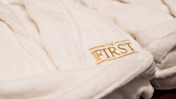 Una pila de toallas blancas con un logotipo dorado bordado que dice "THE FIRST".