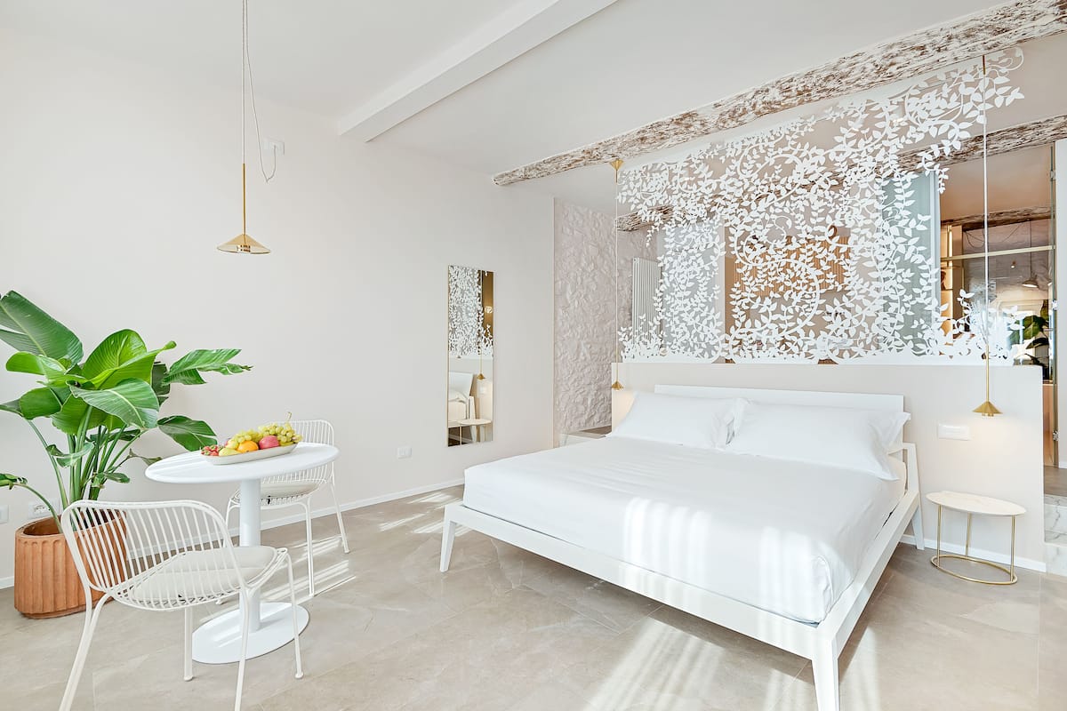 A modern bedroom with a large bed, white furniture, a round dining table, and a potted plant.