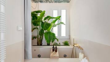 A bathroom with a bathtub, a window, and a plant.