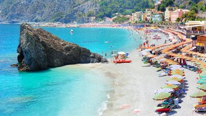 A beach with a rocky outcrop, clear turquoise water, and colorful umbrellas.