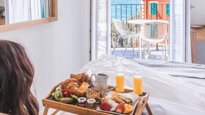 A room with a balcony, a breakfast tray with croissants, fruits, and juice, and a view of a coastal building.