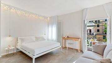 A modern bedroom with a bed, bedside table, chair, and a view of the outside balcony.