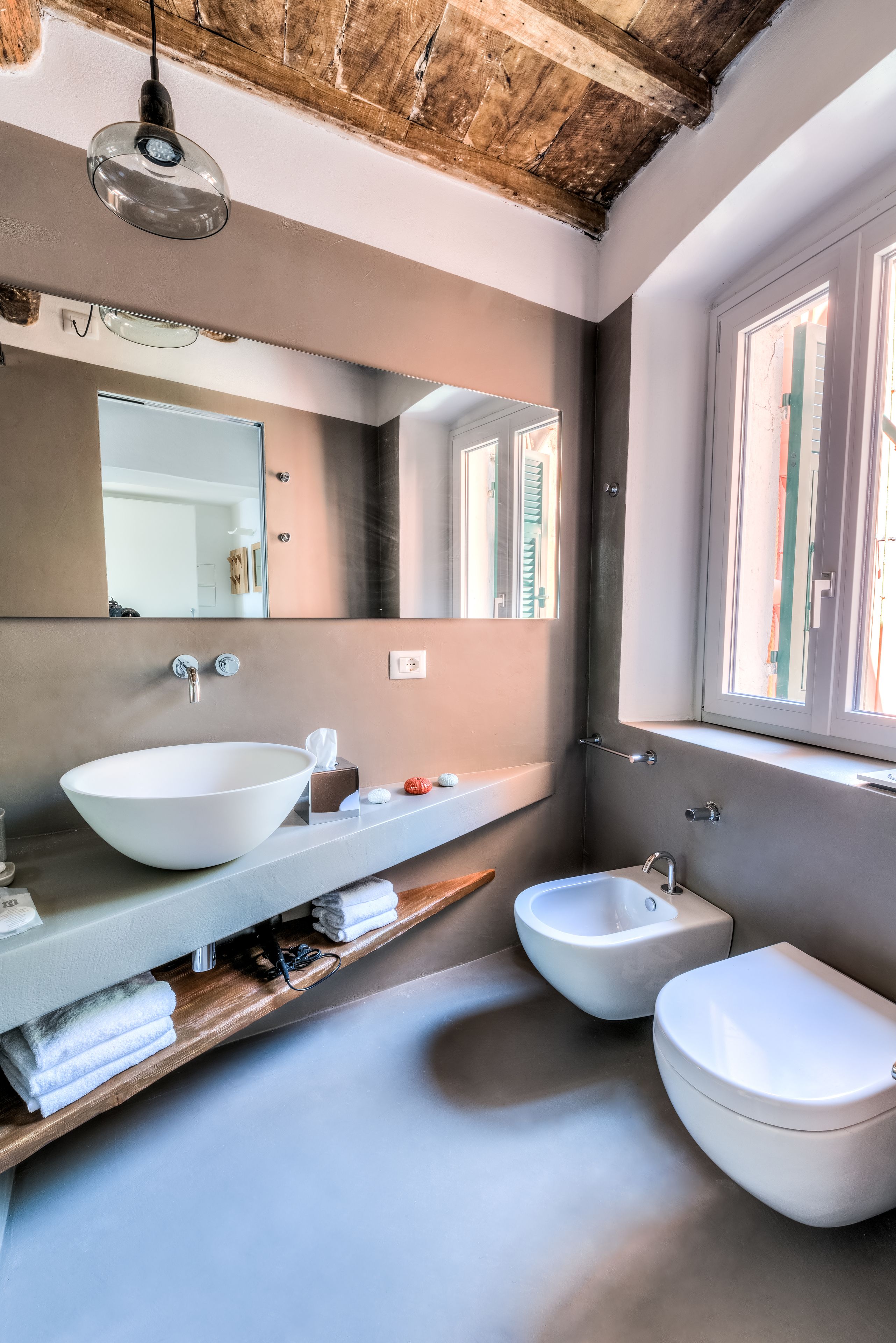 A modern bathroom with a large mirror, a vessel sink, two bidets, and a wooden shelf with towels.