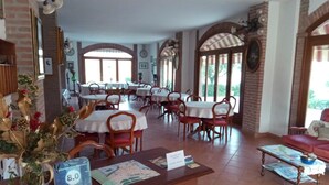 A spacious dining area with multiple tables and chairs, a wooden reception desk, and a view of the outdoors through large windows. - Agriturismo Corte Trincerone (Mantua)