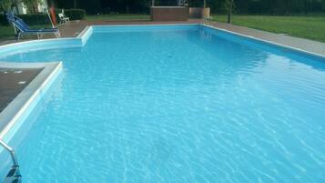 Una piscina rectangular con agua azul cristalina, rodeada por una solana de ladrillo y una zona de césped.