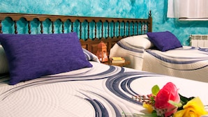 A hotel room with a bed featuring a striped and circular patterned bedspread, two pillows, a nightstand with a book and a lantern, and a bouquet of flowers. - Casa Rural Los Moros (Solosancho)