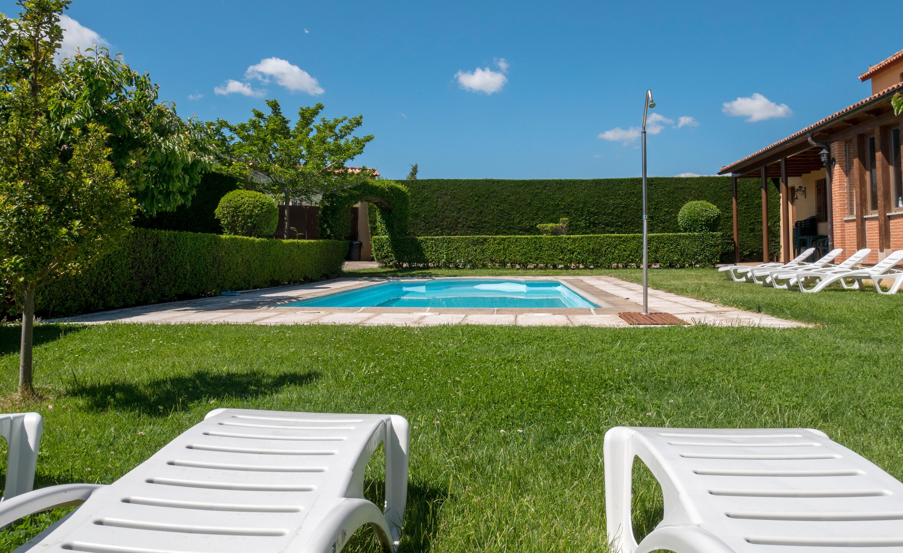 Un espace piscine avec des chaises longues, un ciel dégagé et des haies bien entretenues.