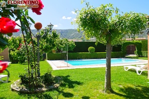 A pool surrounded by well-maintained grass, a few trees, and a lamp post.