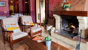 A cozy seating area with two wooden chairs, a table, and a fireplace. - Casa Rural Los Moros (Solosancho)