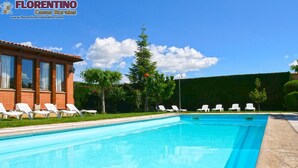 A clear blue swimming pool with white lounge chairs and a red-roofed building. - Casa Rural Los Moros (Solosancho)