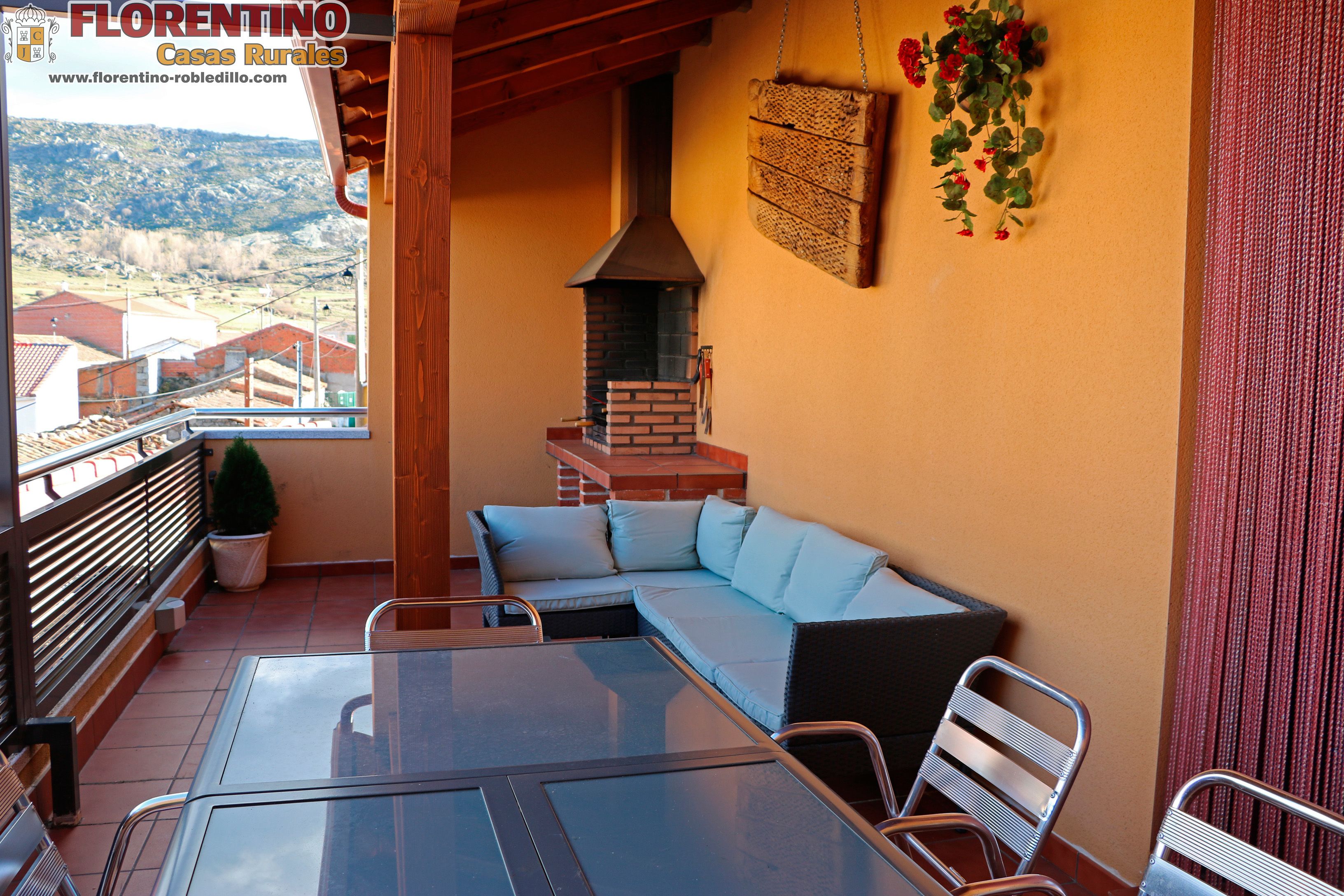 Un patio con mesa de vidrio, sillas de metal, chimenea de ladrillo y un sofá.