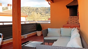 A balcony with a wicker sofa, a small table, and a brick oven. - Casa Rural Los Moros (Solosancho)
