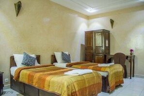A hotel room with two beds, wooden furniture, and a small table with a vase. - Hotel Cabourg (Dakar)