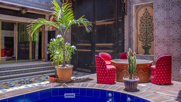 A courtyard with a pool, red upholstered chairs, and potted plants. - Hotel Cabourg (Dakar)